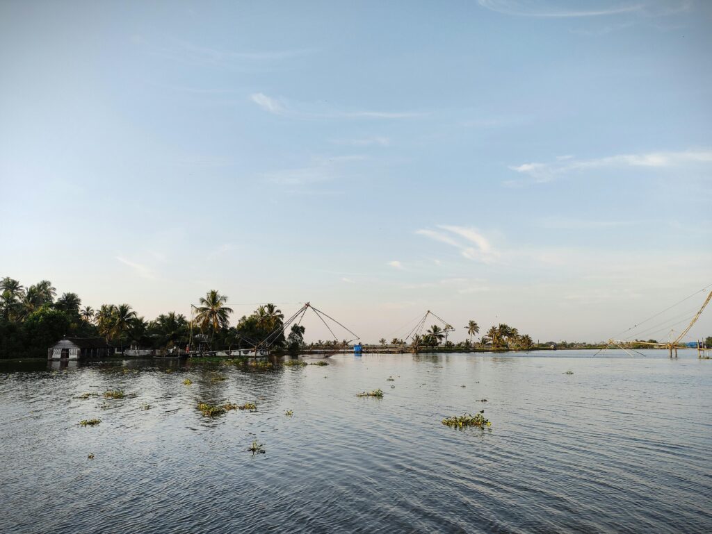 Peaceful view of Kerala backwaters with traditional Chinese fishing nets through calm water and palm trees.